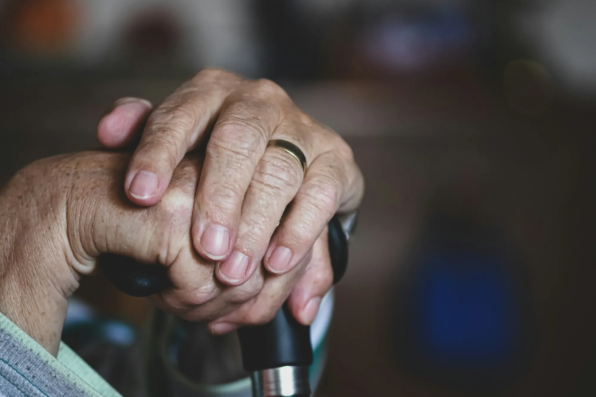 An older person's hands resting on the handle of a walking stick